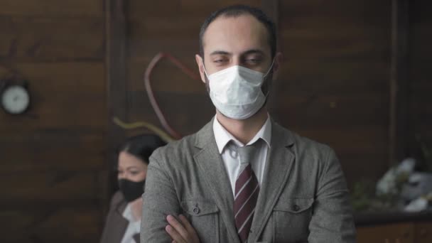 Freelancer hombre en máscara protectora de pie delante de colegas con los brazos cruzados mirando a la cámara. Hombre guapo freelancer trabajando en la oficina durante la cuarentena. Prores 422 — Vídeos de Stock