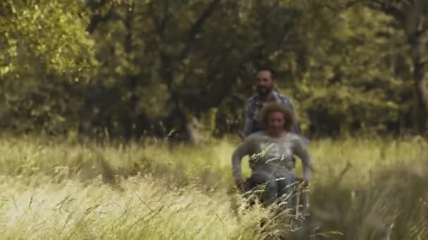 Imagens dentadas. Crianças correndo na frente dos pais, enquanto o pai ajudando a mãe a obter verdadeira grama alta no parque ou quintal. Conceito de pessoas com deficiência. Conceito familiar. Prores 422 — Vídeo de Stock