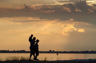 Gün batımında sahilde yürüyen bir ailenin silueti.