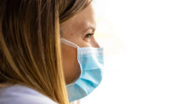 Endişeli, koruyucu kıyafetli bir kadın doktor, hastane penceresinden bakıyor.