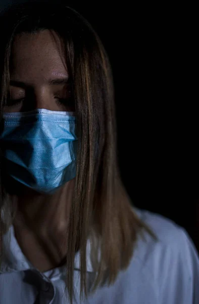 Siyah arka planda, maske takmış ve cerrahi maske takmış genç bir kadın hemşire portresi.