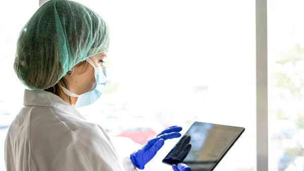 Hastanede dikilirken dijital tablet kullanan tanınmayan bir kadın hemşirenin görüntüsü. Bir maske tak