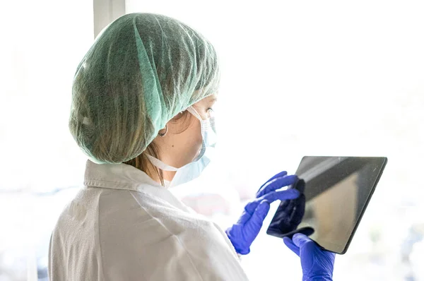 Hastanede dikilirken dijital tablet kullanan tanınmayan bir kadın hemşirenin görüntüsü. Bir maske tak
