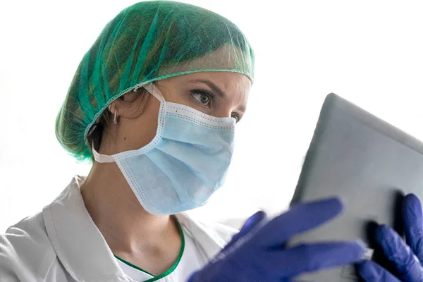 Hastanede dikilirken dijital tablet kullanan tanınmayan bir kadın hemşirenin görüntüsü. Bir maske tak