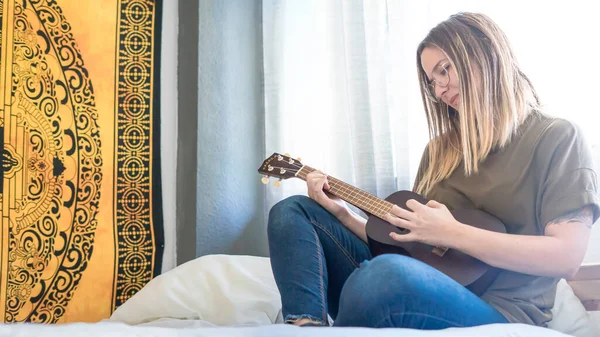 Yatak odasında telli çalgılarla müzik çalan bir kadın. Ukulele Çalıyor