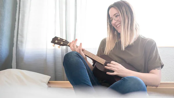 Yatak odasında telli çalgılarla müzik çalan bir kadın. Ukulele Çalıyor