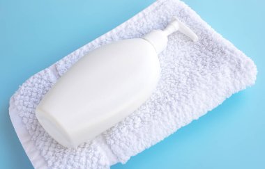 Beyaz şişe ve beyaz havlu mavi arka planda, yakın plan. Spa-cilt bakımı, güzellik, banyo ve banyo kavramı, seçici odaklanma