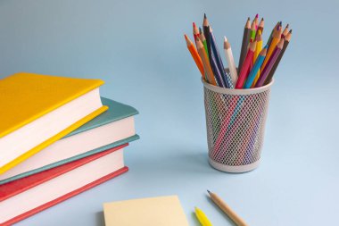 Okula dönelim. Çok renkli kapaklı kitaplar, renkli kalemler, not defterleri ve mavi arka planda bir kalem yığını. Eğitim kavramı. Seçici odak