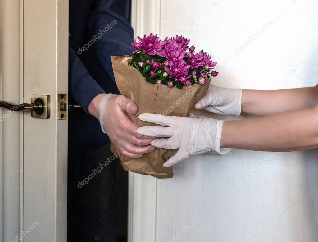 A woman in protective gloves receives a bag of flowers for Mother's Day. Delivery service during the COVIND-19 coronavirus quarantine. Isolation of the population during the pandemic.