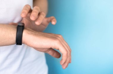 Genç adamın sağ elinde bir fitness bileziği var. Modern sağlık izleme teknolojileri kavramı. Yakın plan, mavi arkaplan, seçici odak, metin alanı