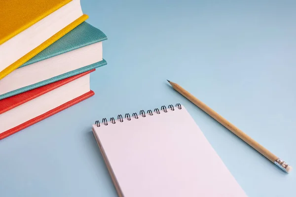 Back to school. Books with bright covers, pencil and Notepad on a blue background. Concept of education.