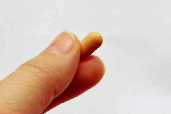 Mão segurando uma pílula entre o polegar e o indicador isolado no fundo branco — Fotografia de Stock