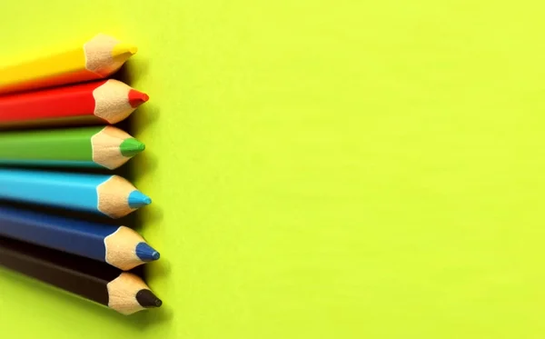 Colored pencils on a yellow background. 6 colors Black, blue, blue, green, red, yellow. Pencils are well-honed. Flatlay. Isolated. Art. Art therapy. Leisure. Pencils are placed on the left