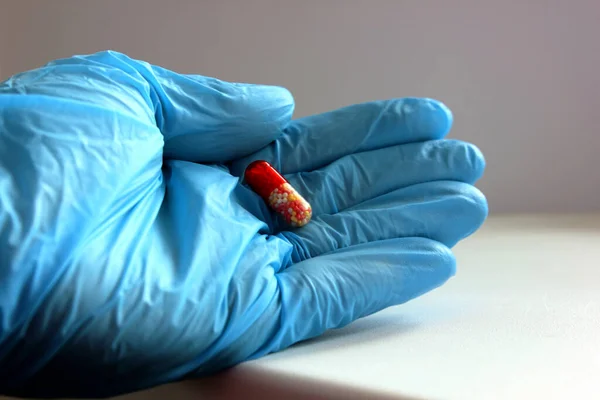 A piros-fehér tabletta a tenyerén nyugszik. Egy kéz egy kék kesztyűben. A bal oldalon van. Droghasználat. Kezelés. Elsősegély doboz. Betegség. Sürgősségi szolgálat. Fénymásolási hely — Stock Fotó