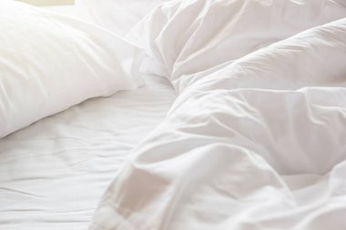Yatak odasındaki kırışık, dağınık battaniye ve beyaz yastık sabah uyandıktan sonra, uzun bir gece uyuduktan sonra, yorgan ve battaniyenin ayrıntıları, otel odasında beyaz battaniyeli yapılmamış bir yatak..