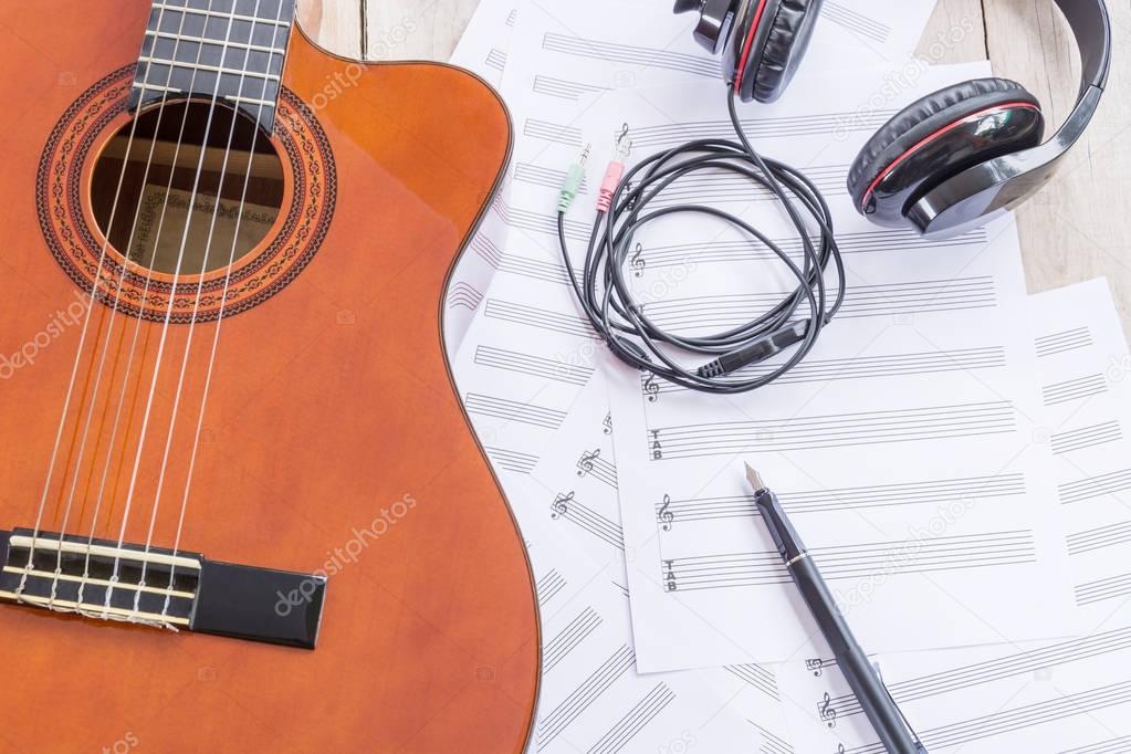 Acoustic guitar, sheet music and fountain pen on wooden table