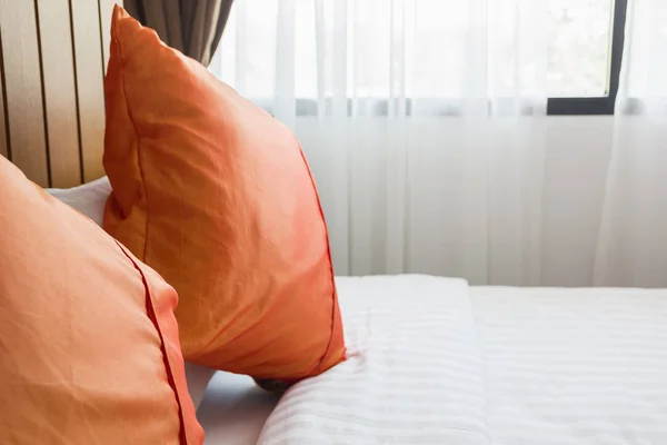 orange pillow and white blanket on bed in bedroom with lighting upper right side