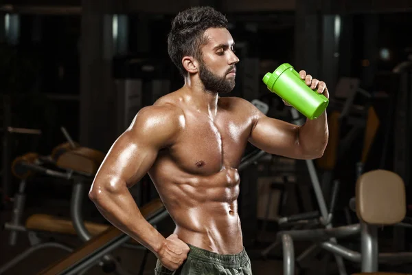 Hombre musculoso sexy bebiendo agua en el gimnasio, en forma abdominal. Fuertes abdominales masculinos desnudos del torso, haciendo ejercicio —  Fotos de Stock