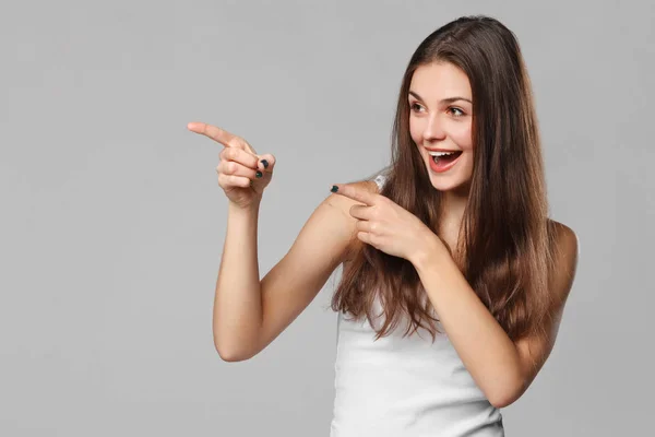 Smiling excited woman showing finger on copy space for product or text, isolated over grey background — Stock Photo, Image