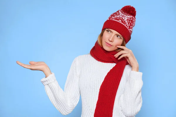 Νεαρή όμορφη γυναίκα σκέφτεται να κοιτάζει προς την πλευρά με την παλάμη δείχνει ανοιχτό χέρι στο κενό αντίγραφο χώρου, Χριστούγεννα κορίτσι φορώντας ζεστό πλεκτό καπέλο και κασκόλ, απομονώνονται σε μπλε φόντο — Φωτογραφία Αρχείου
