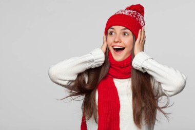 Yana doğru heyecan arayan sürpriz mutlu güzel kadın. Örme sıcak şapka ve atkı, gri arka plan üzerinde izole giyen Noel kız