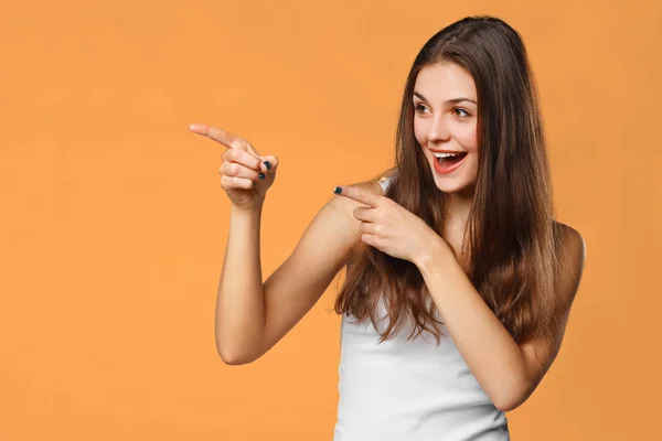 Sonriente mujer emocionada mostrando el dedo en el espacio de copia para el producto o texto, aislado sobre fondo naranja —  Fotos de Stock