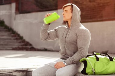 Etkin delikanlı içme suyu, açık havada. Yakışıklı kaslı erkek holding shaker