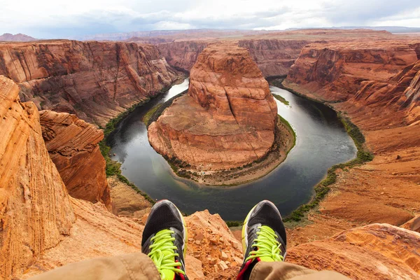 Piernas del viajero sentado en el fondo del cañón Horseshoe bend, Arizona, EE.UU. Concepto de viaje, vista panorámica —  Fotos de Stock