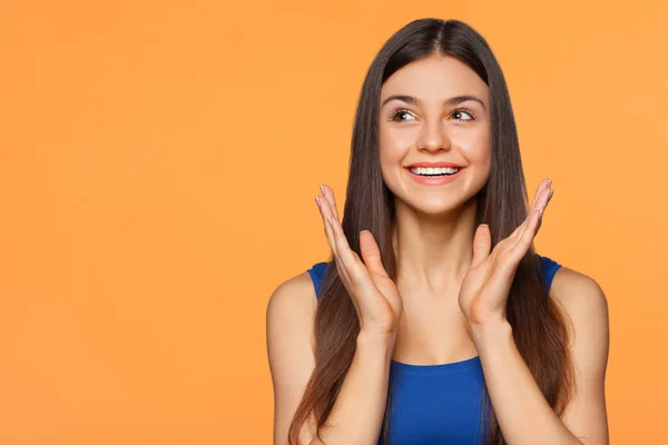 Verbaasd gelukkig mooie vrouw op zoek zijwaarts in opwinding, geïsoleerd op een oranje achtergrond — Stockfoto