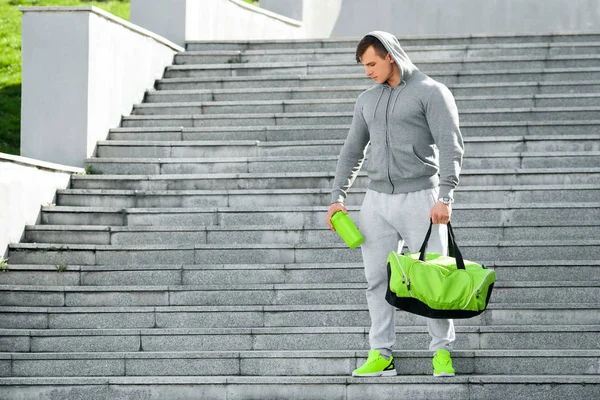 Hombre muscular activo sosteniendo agitador y bolsa de deporte, al aire libre — Foto de Stock