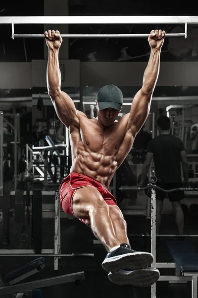Мускулистый мужчина тренируется в спортзале, делает упражнения на животе на горизонтальной полосе, сильный мужской обнаженный пресс для туловища — стоковое фото
