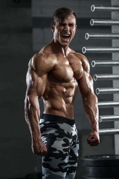 Hombre musculoso mostrando músculos, posando en el gimnasio. Fuertes abdominales masculinos desnudos del torso, haciendo ejercicio —  Fotos de Stock