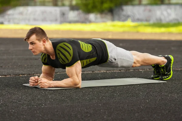 Hombre de fitness haciendo ejercicio de tablón en el estadio, entrenamiento masculino muscular, al aire libre — Foto de Stock