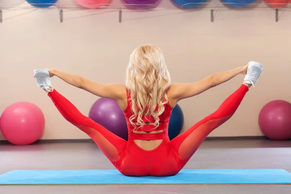 Atletisk flicka gör stretching övning i gymmet. Sport kvinna sitter på en garn. — Stockfoto