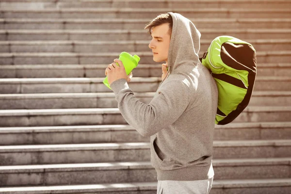 Молодой активный человек пьет воду на открытом воздухе. Красивый мускулистый мужчина держит шейкер — стоковое фото