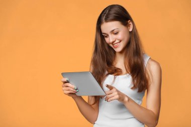 Heyecanlı kız Beyaz gömlekli tablet kullanma. Gülümseyen kadın tablet pc ile üzerinde turuncu arka plan izole