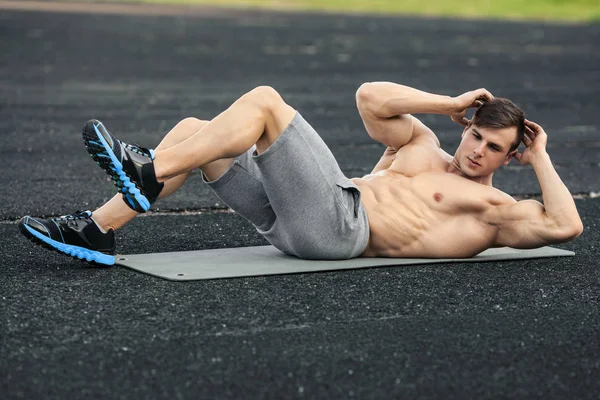 Fitness man doing sit ups in the stadium working out. Muscular male exercising abdominals, outdoor — Stock Photo, Image