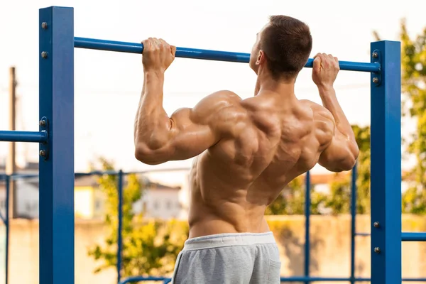 Gespierde man doen van pull up op horizontale balk, uit te werken. Sterke fitness man omhoog te trekken, waaruit terug, buiten — Stockfoto