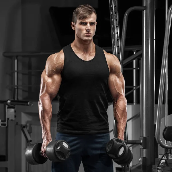 Hombre musculoso ejercitándose en el gimnasio haciendo ejercicios, macho fuerte con mancuernas —  Fotos de Stock