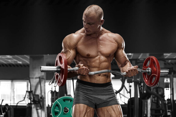 Muscular man working out in gym doing exercises with barbell, strong male naked torso abs