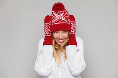 Yana doğru heyecan arayan şaşırmış mutlu kadın. Örme sıcak şapka ve gri arka plan üzerinde izole eldivenler giymiş Noel kız