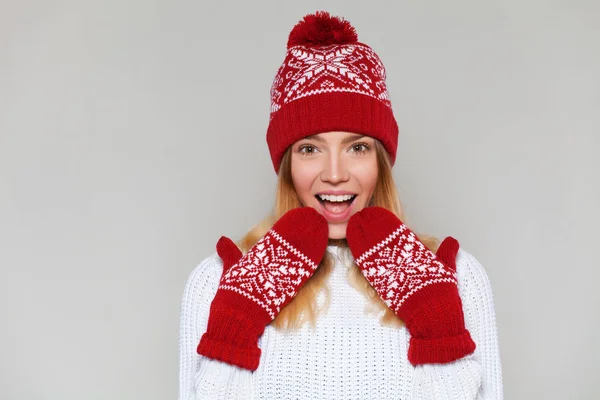 Έκπληκτος ευτυχισμένη γυναίκα κοιτάζοντας λοξά σε ενθουσιασμό. Χριστούγεννα κορίτσι φορώντας ζεστό πλεκτό καπέλο και γάντια, απομονώνονται σε γκρίζο φόντο — Φωτογραφία Αρχείου