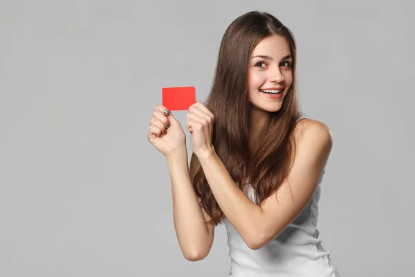 灰色の背景の上分離した白い シャツで空白のクレジット カードを見せて女性の笑みを浮かべて — ストック写真