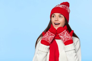 Heyecanlı kadın yana doğru heyecan arıyorum. Örme sıcak şapka ve atkı, mavi izole giyen sürpriz Noel kız