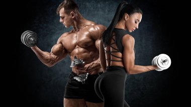 Dambıllarla spor yapan bir çift. Kaslı adam ve kadın kaslarını gösteriyor.
