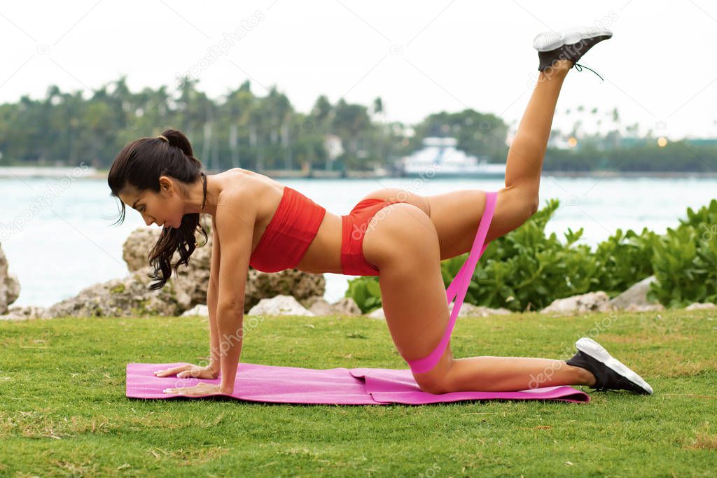 Athletic woman workout with resistance band outdoors. Fitness girl doing exercise for glutes at the park