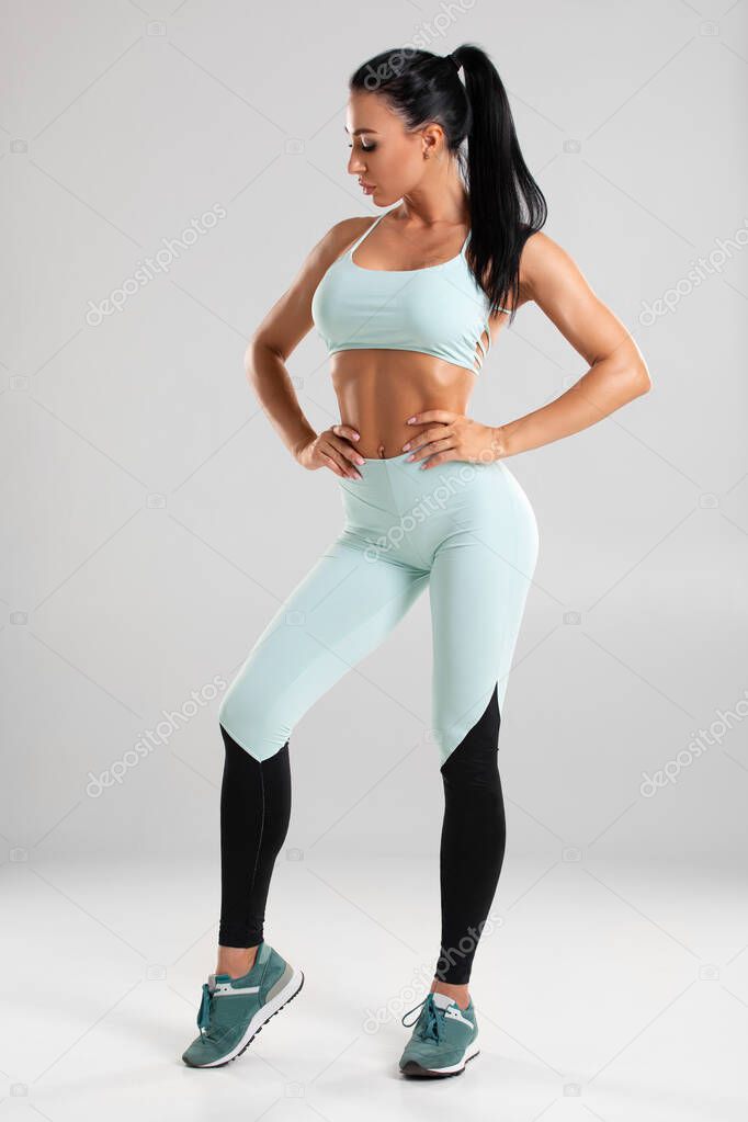 Beautiful athletic girl, sexy fitness woman in leggings on the gray background