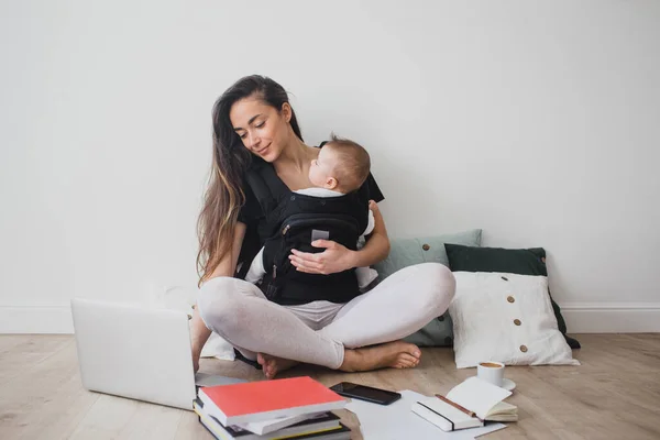 Mother working at home with baby in ergo backpack