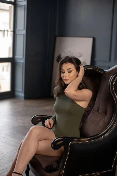 Piękna brunetka w sexy zielony body z nagie nogi siedzi — Zdjęcie stockowe