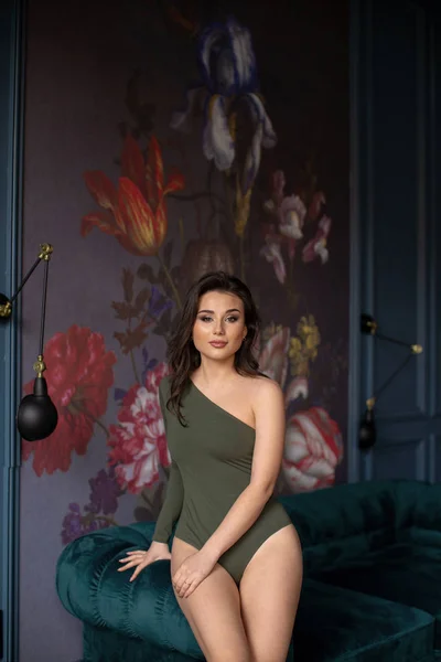 Soffa 'nın yanında çıplak bacaklı, yeşil elbiseli seksi esmer. — Stok fotoğraf